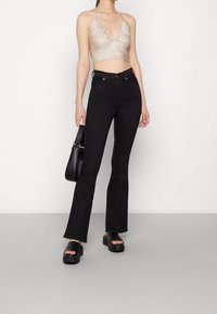 Metalický zlatý halter crop top spárovaný s černými vysokými zvonovými džíny a černými platformovými sandály. Modelka drží černou kabelku.