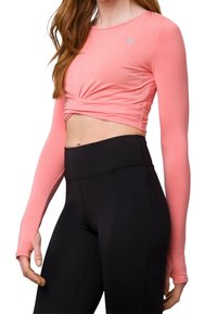 Světle růžový krátký top s dlouhým rukávem z hladké látky má přední design s kroucením, doplněný o legíny s vysokým pasem v černé barvě.