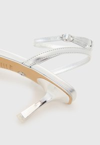 Silvriga högklackade sandaler med korsade remmar, metallisk finish, spetsig tå och en slät, glansig klack.