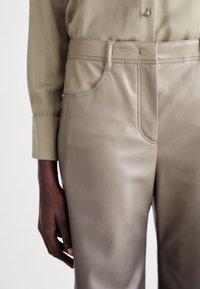 Beige faux læder bukser med en tætsiddende design, med stikninger, lommer og en glat overflade, parret med en grøn skjorte.