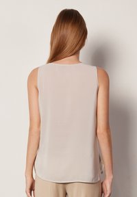 Ljus beige ärmlös blus med en mjuk, flödande textur. Rundad halsringning och sidoklyftor vid fållen. Sömlös baksidedesign.