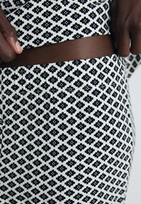 Close-up of dark-skinned hands adjusting black and white floral patterned waistband on matching fabric clothing.