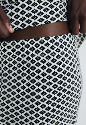 Close-up of dark-skinned hands adjusting black and white floral patterned waistband on matching fabric clothing.