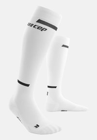 Calze compressive bianche con accenti neri. Presentano una texture a coste, un design al ginocchio e un logo stampato lungo il lato.