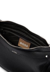 Borsa a tracolla in pelle nera con superficie texture. Presenta dettagli in argento, multi-scomparti e un'etichetta del marchio visibile all'interno.