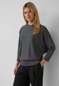 Grijze gebreide pullover met een ronde hals, verlaagde schouders en geribde zoom. Zachte textuur en een ruime pasvorm, gecombineerd met zwarte broek.