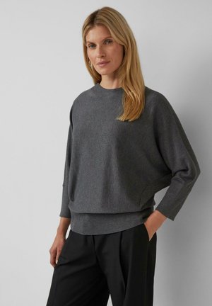 Grijze gebreide pullover met een ronde hals, verlaagde schouders en geribde zoom. Zachte textuur en een ruime pasvorm, gecombineerd met zwarte broek.