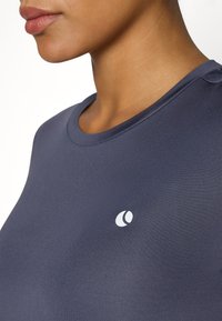 Marineblauw sportt-shirt met een ronde halslijn, gemaakt van een gladde stof. Heeft een klein wit logo aan de linkerkant, vlakbij de zoom.