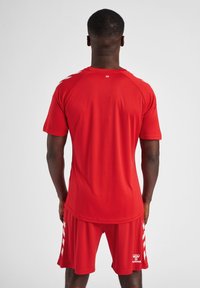 Jersey atlético rojo con mangas cortas y pantalones cortos a juego, con una textura suave y rayas blancas de acento en los laterales.