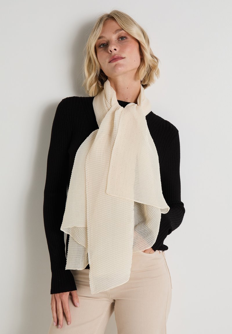 Bufanda de color crema con tela texturizada y acanalada. Colocada de manera casual alrededor del cuello, presenta bordes suaves y un diseño en capas.