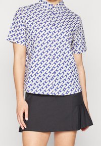 Košile s krátkým rukávem na knoflíky s geometrickým modro-bílým vzorem, s špičatým límcem a mírně volným střihem.