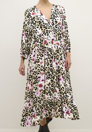 Długa sukienka w panterkę z różowymi i czerwonymi kwiatowymi wzorami, z rękawami do połowy przedramienia, dekoltem w serek i falbaną u dołu, noszona z czarnymi botkami za kostkę.