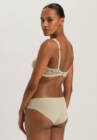 Vaalea beige pitsinen rintaliivi säädettävillä olkaimilla ja hakasulkimella, yhdistettynä samanlaisiin saumattomiin keskikorkeisiin alushousuihin. Silkkinen rakenne ja hienovarainen muotoilu.