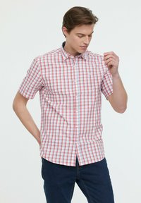 Chemise à boutons à manches courtes avec un motif à carreaux rouge et bleu sur fond blanc. Le tissu semble léger et offre une coupe décontractée.