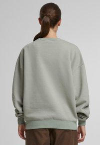Lys grønn oversized sweatshirt med ribbede mansjetter og hem, laget av myk stoff. Har fallende skuldrer og rund hals.