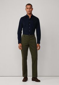 Marineblauw overhemd met lange mouwen, gecombineerd met olijfgroene broek. Bruine schoenen maken de outfit af. Simpel, tailleren ontwerp.