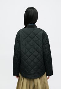 Chaqueta negra acolchada con cuello acanalado y detalles cosidos, con un ajuste holgado y tela texturizada. Vista trasera mostrada.