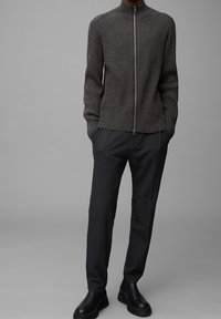 Sweter z ciemnoszarej przędzy, zapinany na zamek, o prążkowanej fakturze i wysokim kołnierzu, w zestawieniu z ciemnymi spodniami i czarnymi botkami za kostkę.