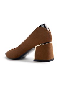 Zapato de tacón alto de ante marrón con un tacón grueso, que presenta un acento negro brillante en la parte trasera y un diseño de punta redondeada.