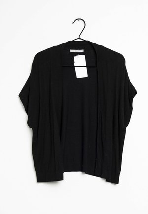 Schwarzer kurzärmeliger, vorne offener Cardigan, der an einem schwarzen Kleiderbügel mit weißem Preisschild vor weißem Hintergrund hängt.