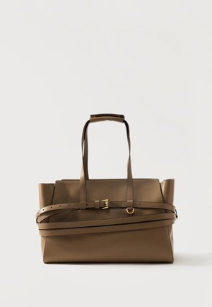 Sac cabas en cuir marron avec double poignée et une sangle de ceinture réglable enroulée autour de son corps, posé sur un fond clair uni.