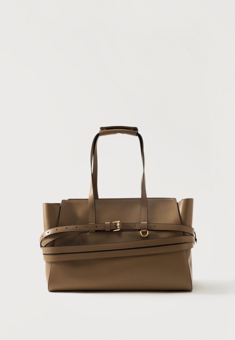 Sac cabas en cuir marron avec double poignée et une sangle de ceinture réglable enroulée autour de son corps, posé sur un fond clair uni.