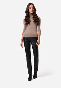 Beige coltrui met korte mouwen, gecombineerd met zwarte leren broek en enkellaarsjes met hak. Eenvoudig en aansluitend ontwerp.