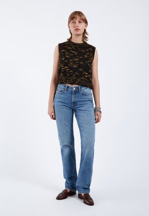 Schwarzes und gelbes, gestricktes, ärmelloses Oberteil, kombiniert mit hochgeschnittenen, hellblauen Jeans aus Denim, mit geradem Bein und subtilen Fransen am Saum.