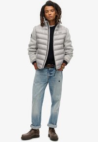 Veste matelassée gris clair avec un corps en polaire grise, un pull foncé, un jean bleu, des bottes marron et une coupe décontractée. Comprend une fermeture éclair et des poches.