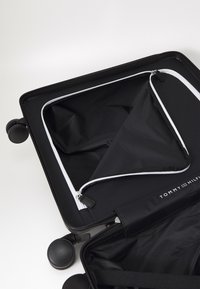 Black suitcase with a textured exterior, white zipper accents, and a divided interior. Features four black wheels for mobility.