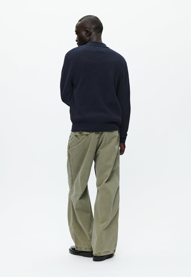 Maglione lavorato a maglia di colore navy e pantaloni larghi di un verde oliva chiaro. Il maglione presenta un motivo testurizzato, mentre i pantaloni hanno una vestibilità rilassata e cuciture visibili.