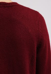 Burgundská pletená svetr s texturovaným povrchem, kulatým výstřihem a bezšvovým designem ramen. Měkký materiál s útulným vzhledem.