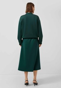 Dunkelgrünes zweiteiliges Outfit, bestehend aus einem lässigen Sweatshirt und einem Midirock, aus weichem, glattem Stoff, mit langen Ärmeln und einfachem Design.