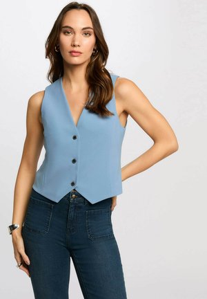 Gilet senza maniche di un azzurro chiaro con scollatura profonda a V, caratterizzato da tre bottoni neri, tessuto texture e vestibilità sartoriale, abbinato a jeans scuri.