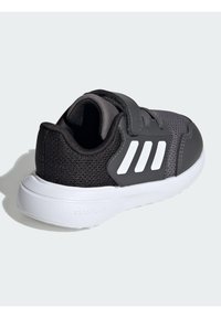 Černá sportovní bota s síťovaným svrškem, suchým zipem a třemi bílými pruhy po straně. Bílá gumová podrážka s texturovaným vzorem pro lepší přilnavost.