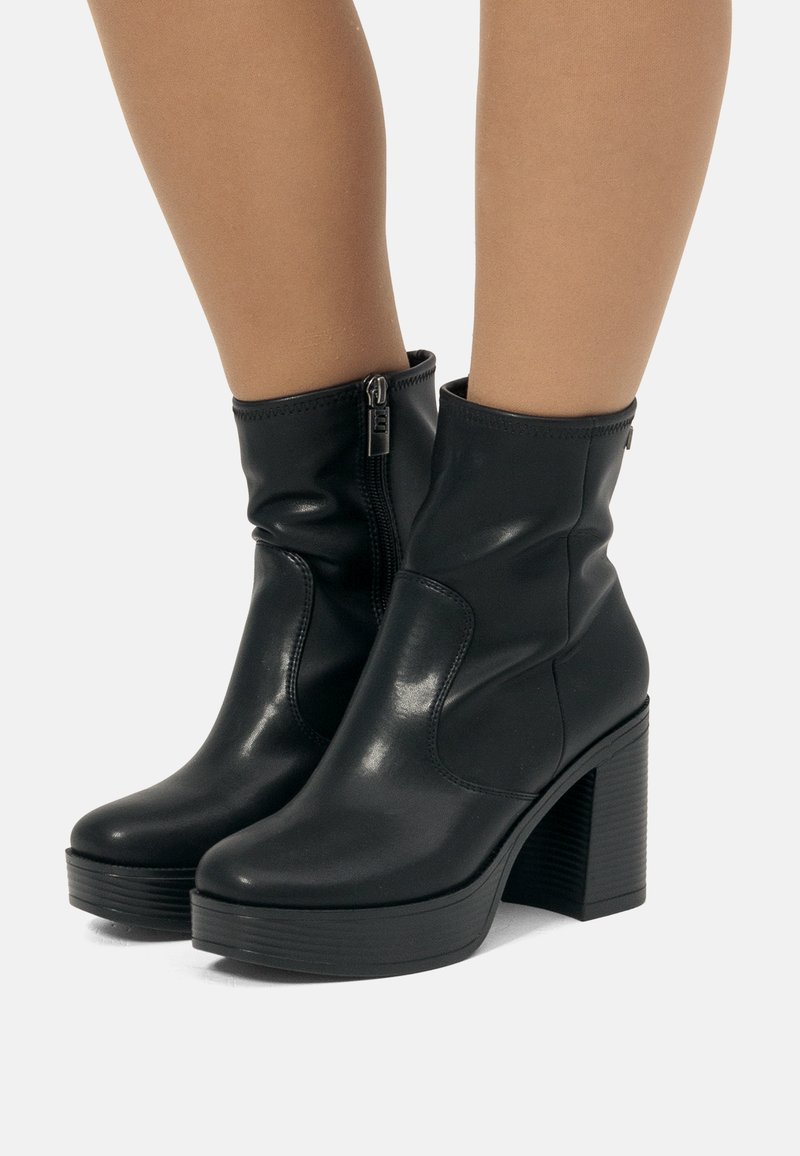 Botas negras hasta el tobillo hechas de cuero suave con puntera redonda, cremallera lateral y un tacón alto y robusto de textura estriada.