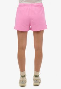 Roze katoenen shorts met een elastische tailleband, een rafelige zoom en zijzakken. Draag ze met lichte sneakers en sokken met groene accenten.