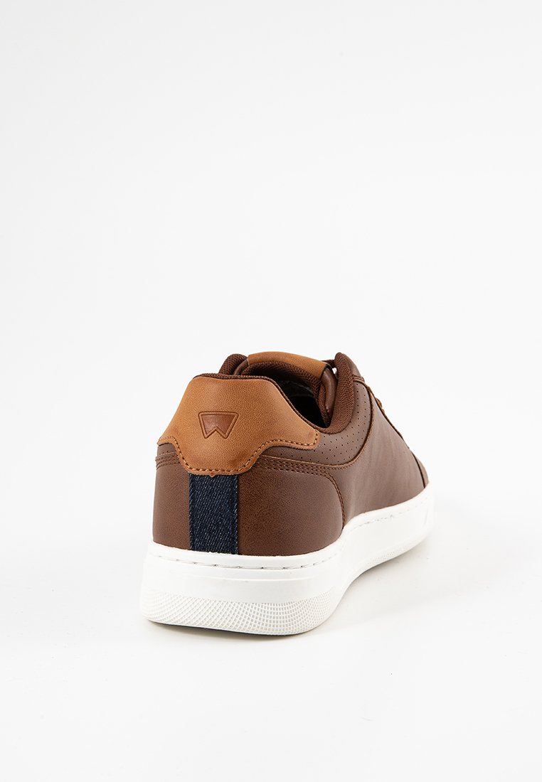 Zapatilla de cuero marrón con un acento en el talón color crema y una franja de denim. Presenta una superficie texturizada y suela de goma blanca. El diseño es de tipo bajo.