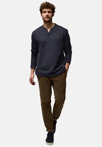 Námořnické dlouhé rukávy henley tričko se třemi knoflíky, v kombinaci s hnědými slim-fit kalhotami. Model má na sobě tmavé tenisky, což vytváří uvolněný vzhled.