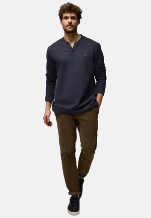 Mørkeblå langærmet henley skjorte med tre knapper, bærer sammen med brune slim-fit bukser. Modellen har mørke sneakers på, hvilket skaber et afslappet look.