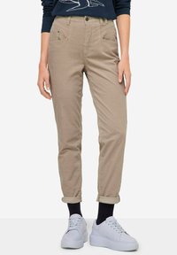 Pantaloni di cotone beige con una vestibilità affusolata, dotati di due tasche frontali e orli arrotolati, abbinati a sneakers bianche.