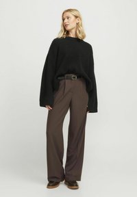 Suéter negro de punto con un corte amplio y relajado; combinado con pantalones marrones de tiro alto, que incluyen un cinturón y botas marrones gruesas.