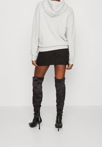 Felpa grigia oversize, minigonna nera in suede e stivali neri sopra il ginocchio con tacco alto. Texture liscia e silhouette aderente.