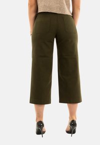 Pantalons cropped verts olive en tissu lisse, dotés de deux poches arrière et d'une coupe droite, associés à des talons hauts noirs.
