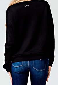 Sweatshirt noir avec un col rond, des manches longues et un petit logo "Guess" blanc dans le dos. Assorti avec un jean en denim bleu.