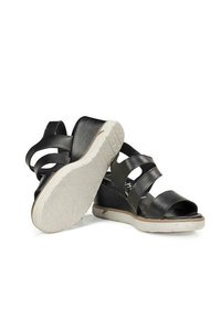 Sandalias de cuña de cuero negro con tres correas ajustables, que cuentan con una suela de goma blanca y una textura en la suela para un mejor agarre.