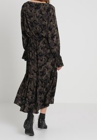 Långärmad klänning i svart och grön camouflage med insydd midja, utsvängd nederdel och volangärm, tillverkad av lätt material.