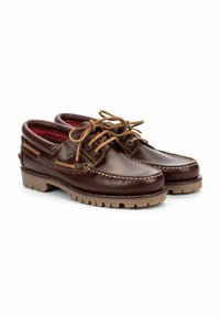 Zapatos de barco de cuero marrón con un acabado suave, detalles de costura, cordones beige y suelas de goma con un patrón de agarre. Forro interior rojo.