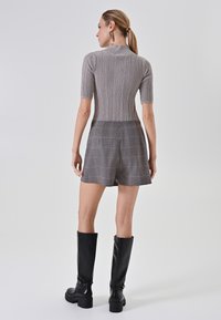 Maglione grigio a coste con maniche corte abbinato a pantaloni corto a vita alta in un motivo a quadri nei toni del grigio e dell'arancione, completato da stivali neri fino al ginocchio.