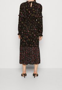 Abito nero floreale con maniche lunghe, dettagli a ricciolo e apertura a chiave sul retro. Presenta piccoli motivi floreali multicolori su una silhouette fluida.
